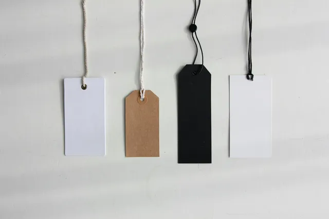 Four blank paper price tags hanging on strings against a pale background