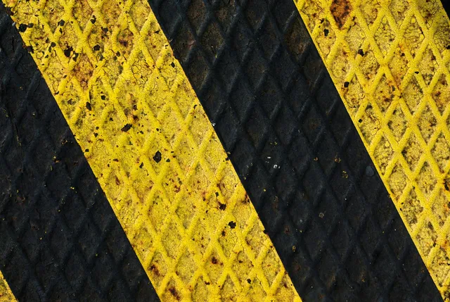 A weathered metal plate painted with diagonal yellow and black hazard stripes