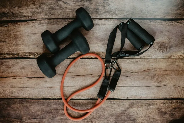 Two dumbbells, an orange resistance band and a pair of handles laid out together on a wooden floor