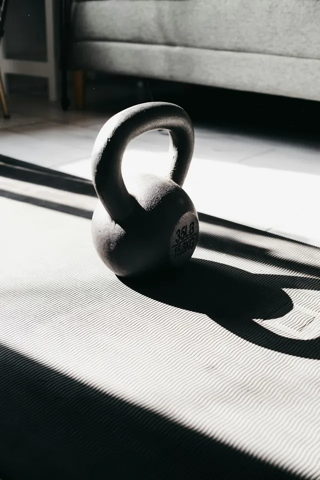 A cast iron kettlebell standing on an exercise mat in low sunlight, at floor level